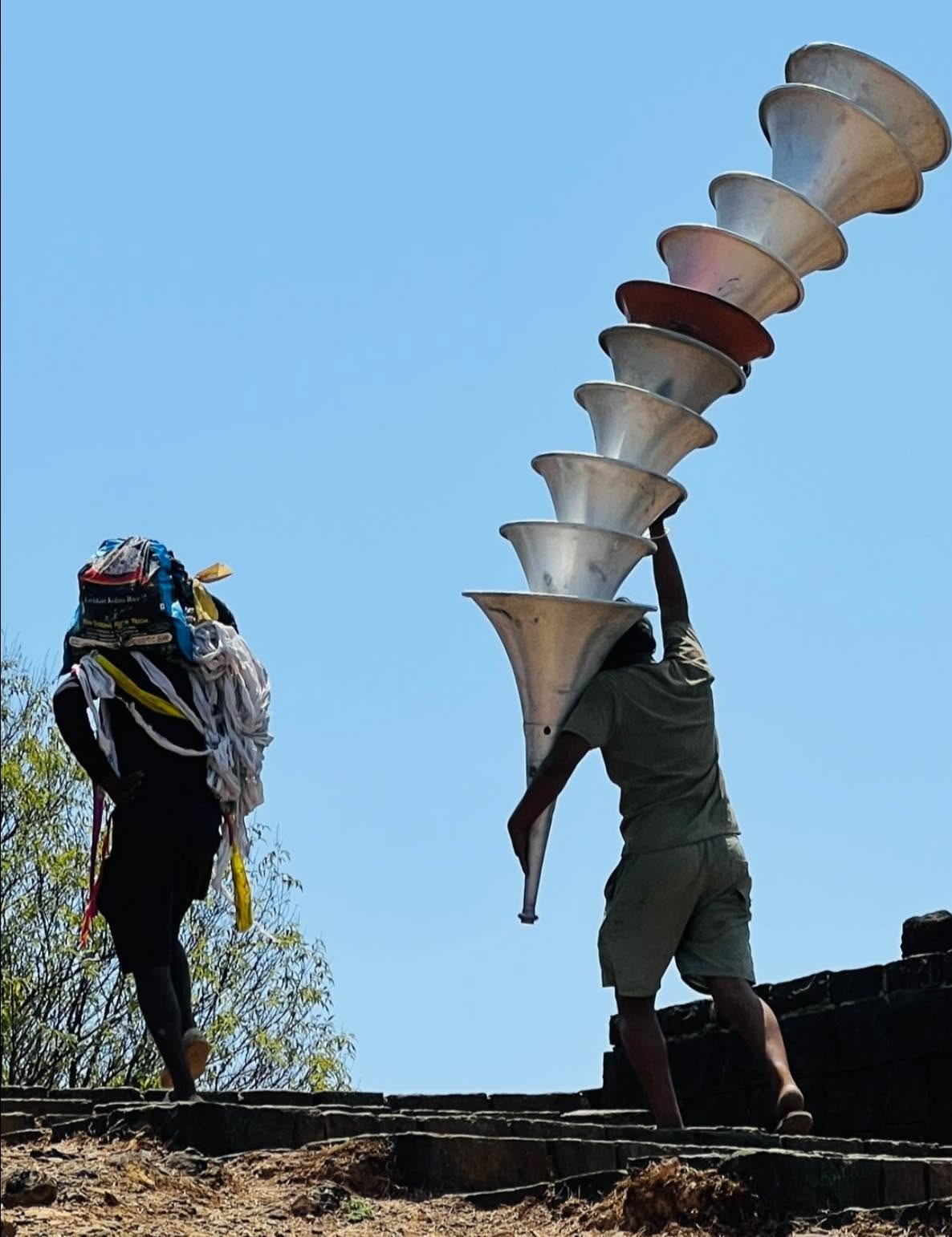 Crew member hand-carrying a stack of speaker horns up the stone steps of Raigad Fort